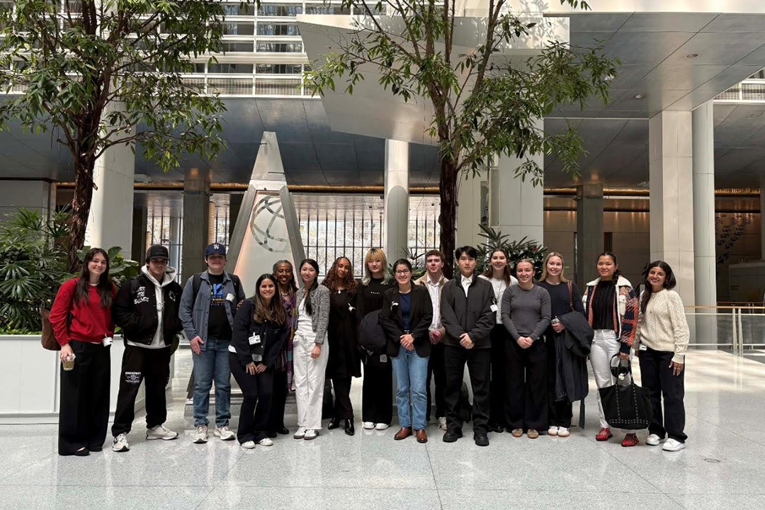 A large group of students standing with Professor Gelaya Debebe in a marble-floored atrium