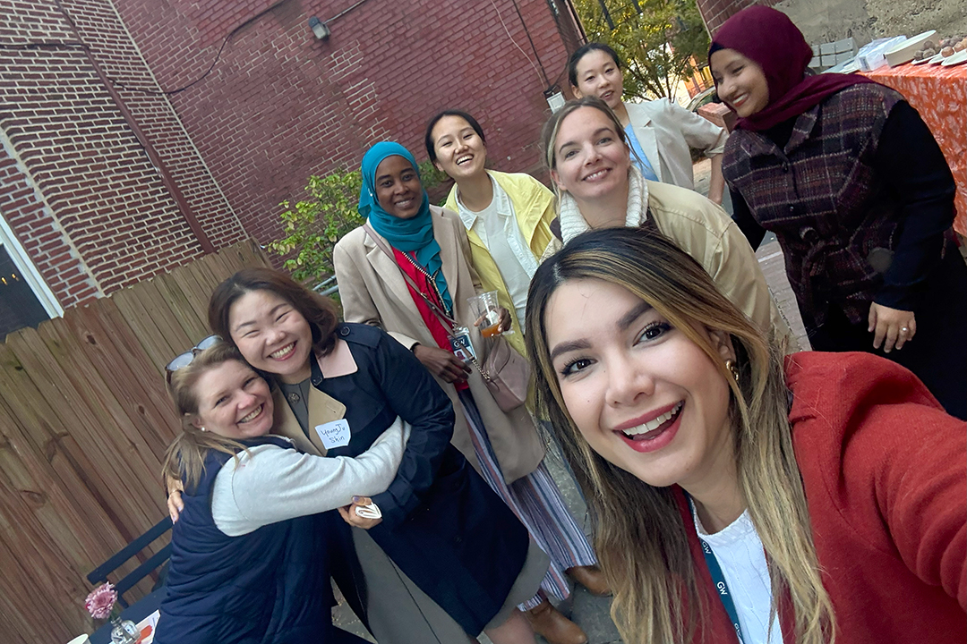 A selfie of a group of students and a professor outside a brick campus building