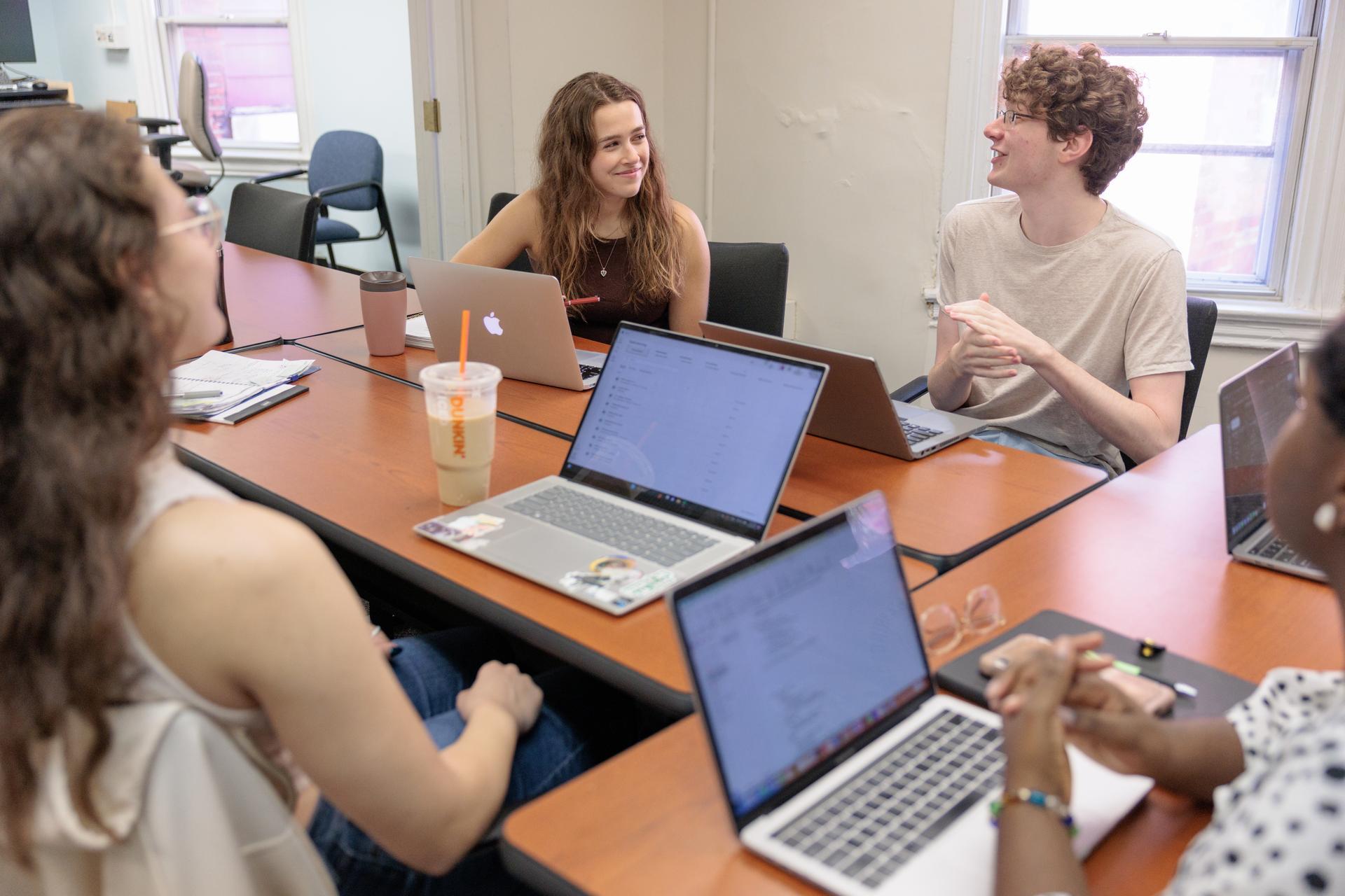 Students in an Org Sci classroom sharing a table and talking with laptops in front of them