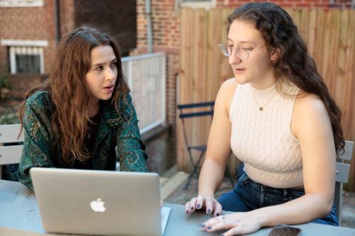Two people seated outside in front of a laptop talking