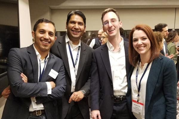 A group of four students in business suits smiling at a conference